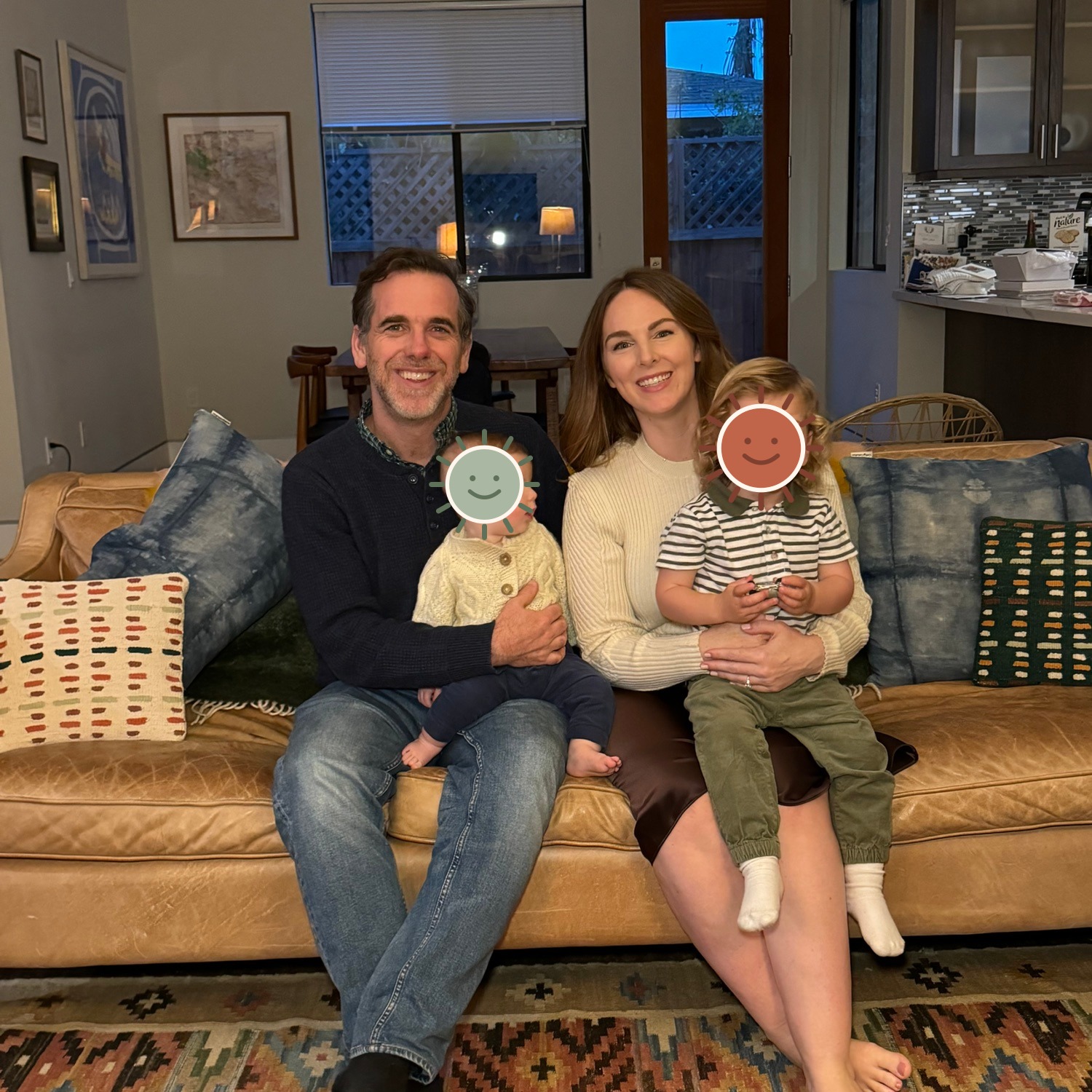 Michael and Hadley sitting on the couch with Henry and baby Luke, whose faces are covered by illustrated stickers for privacy.